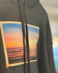 Gray hoodie with a sunset over water patch on a blurred indoor background