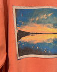 Orange sweatshirt with a photo of a sunset over a lake.