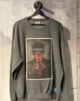 Gray sweatshirt with a graphic print of a person smoking a cigarette, hanging on a wooden surface.