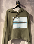 Green hoodie with a printed design of a lake on a hanger against a textured wall.