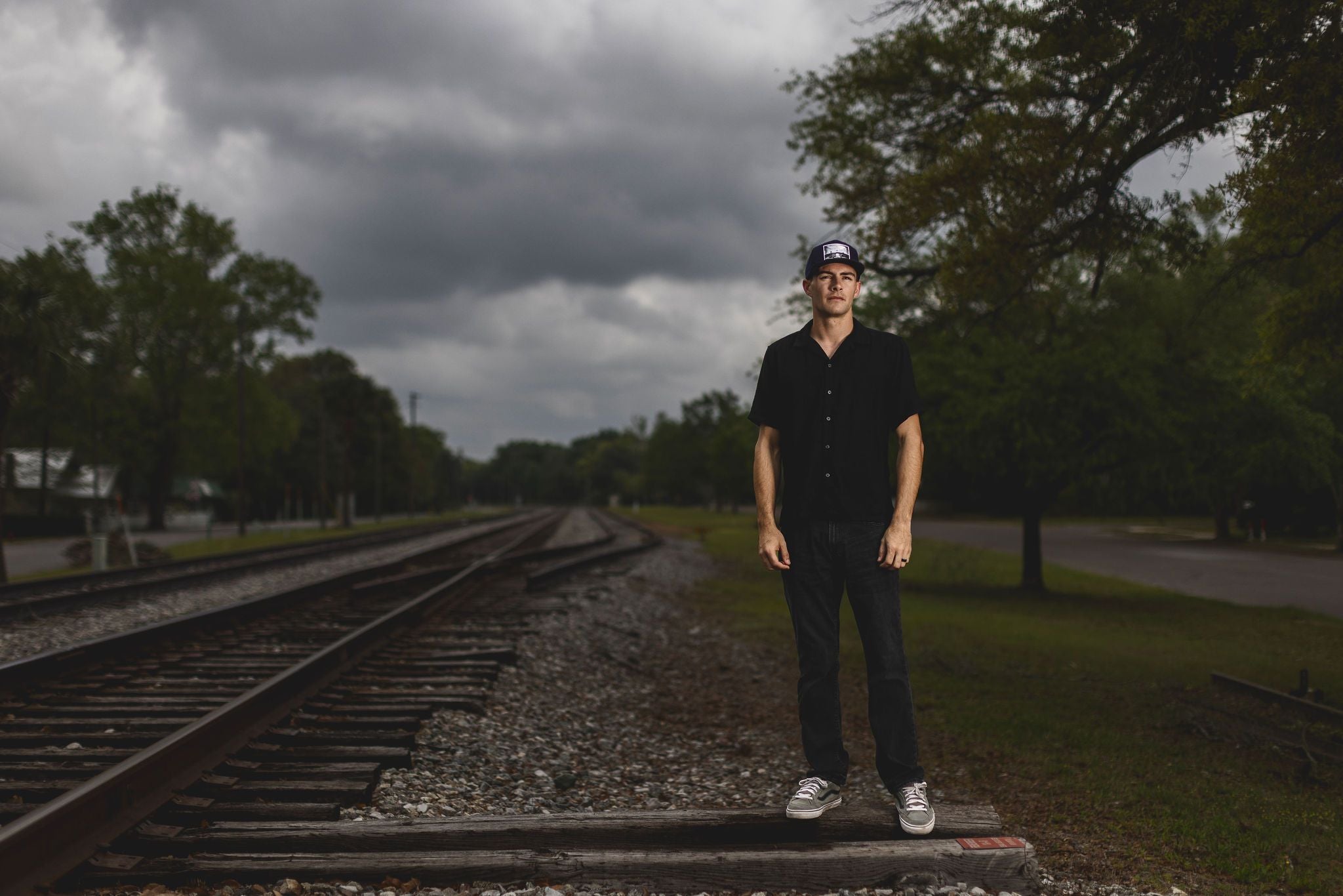 male model wearing a take me to church hat in black with a cloudy background at a train track