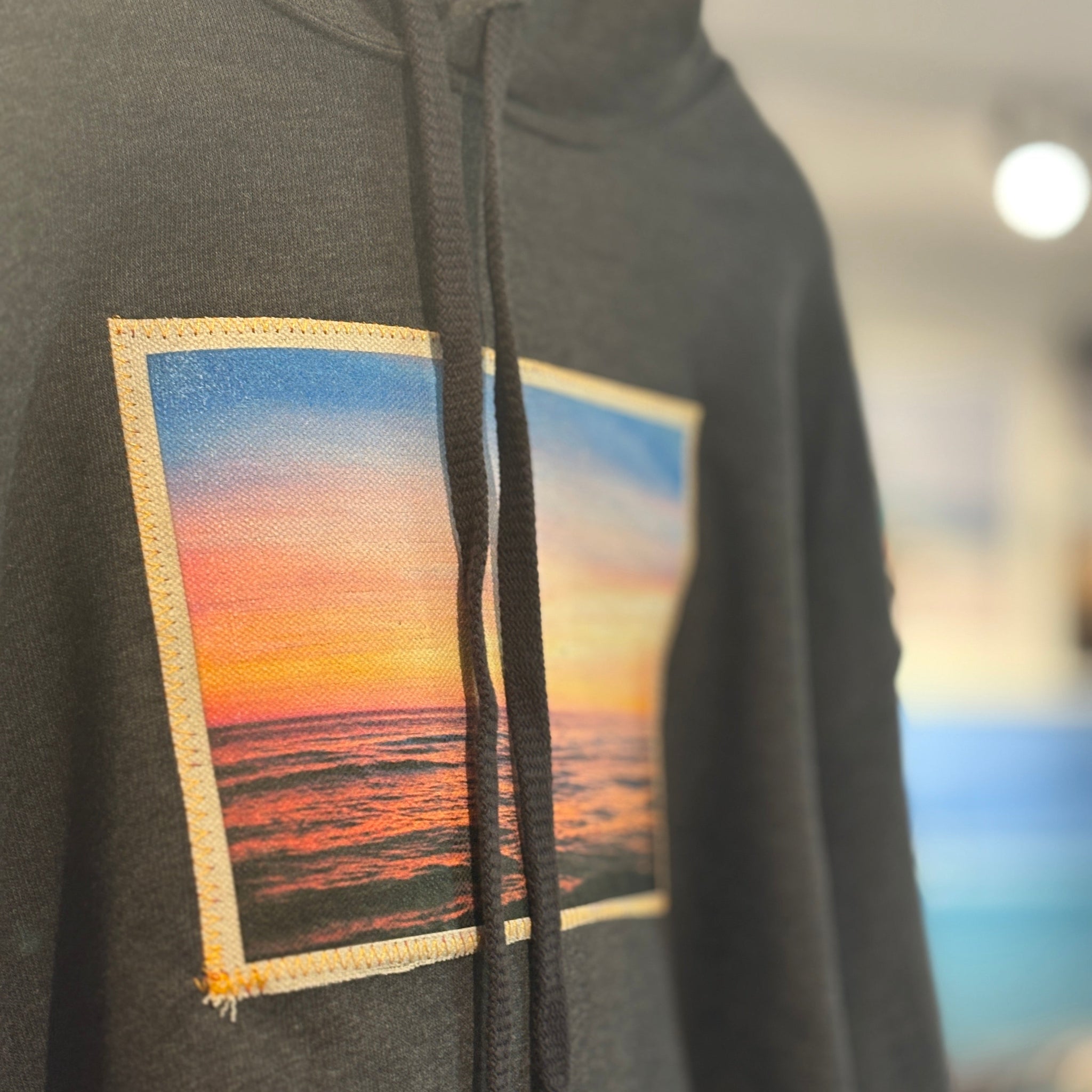Gray hoodie with a sunset over water patch on a blurred indoor background