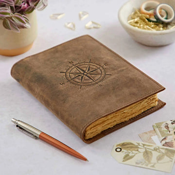 Brown leather notebook with compass design on a light surface with a pen and decorative items.