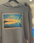 Gray hoodie with a graphic design of a sunset and clouds on a hanger.