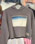 Gray hoodie with a beach graphic on a hanger against a blurred store background