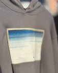 Gray hoodie with a colorful patch on a hanger