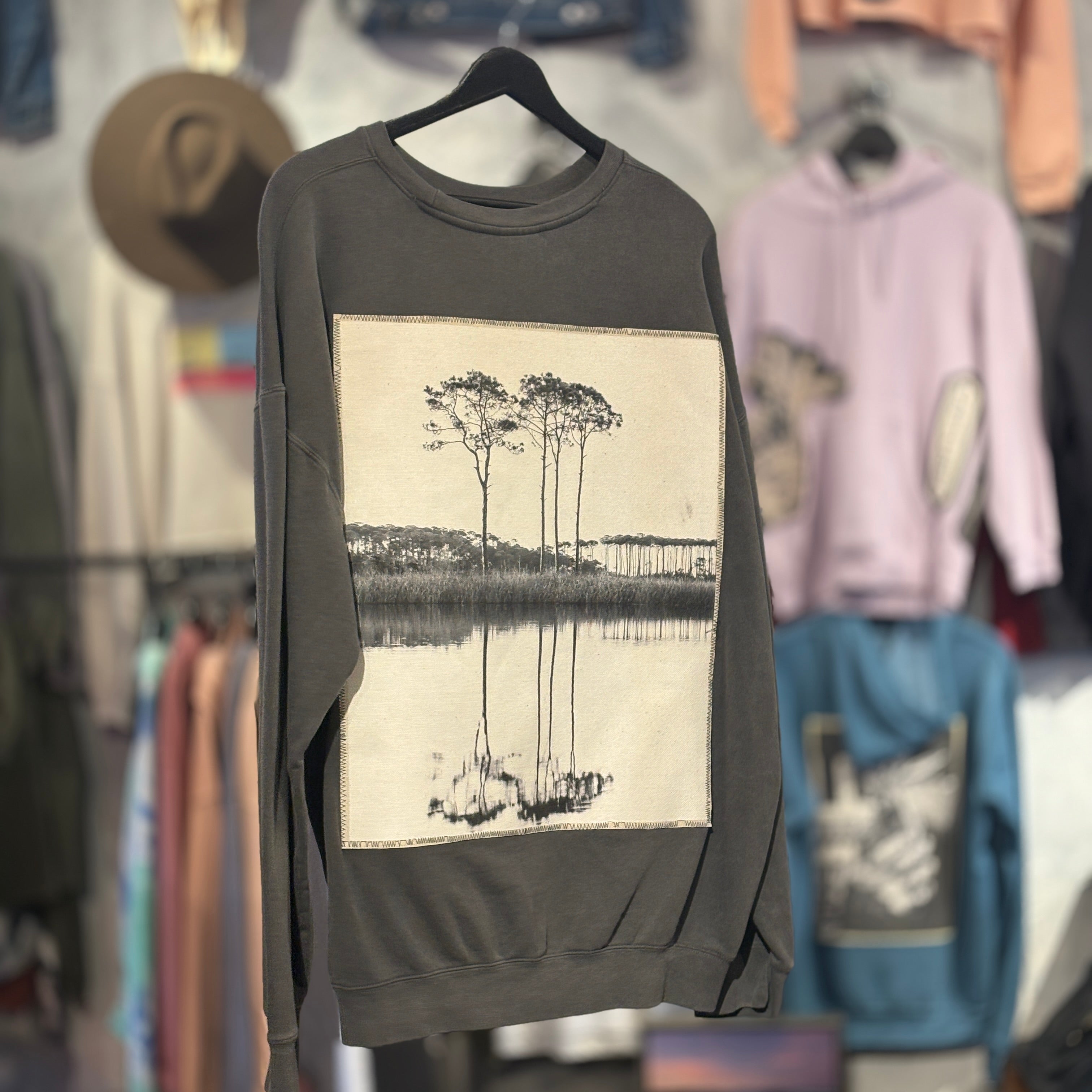 Gray sweatshirt with B&W photo of trees and a lake.  Hanging against blurred background of store.
