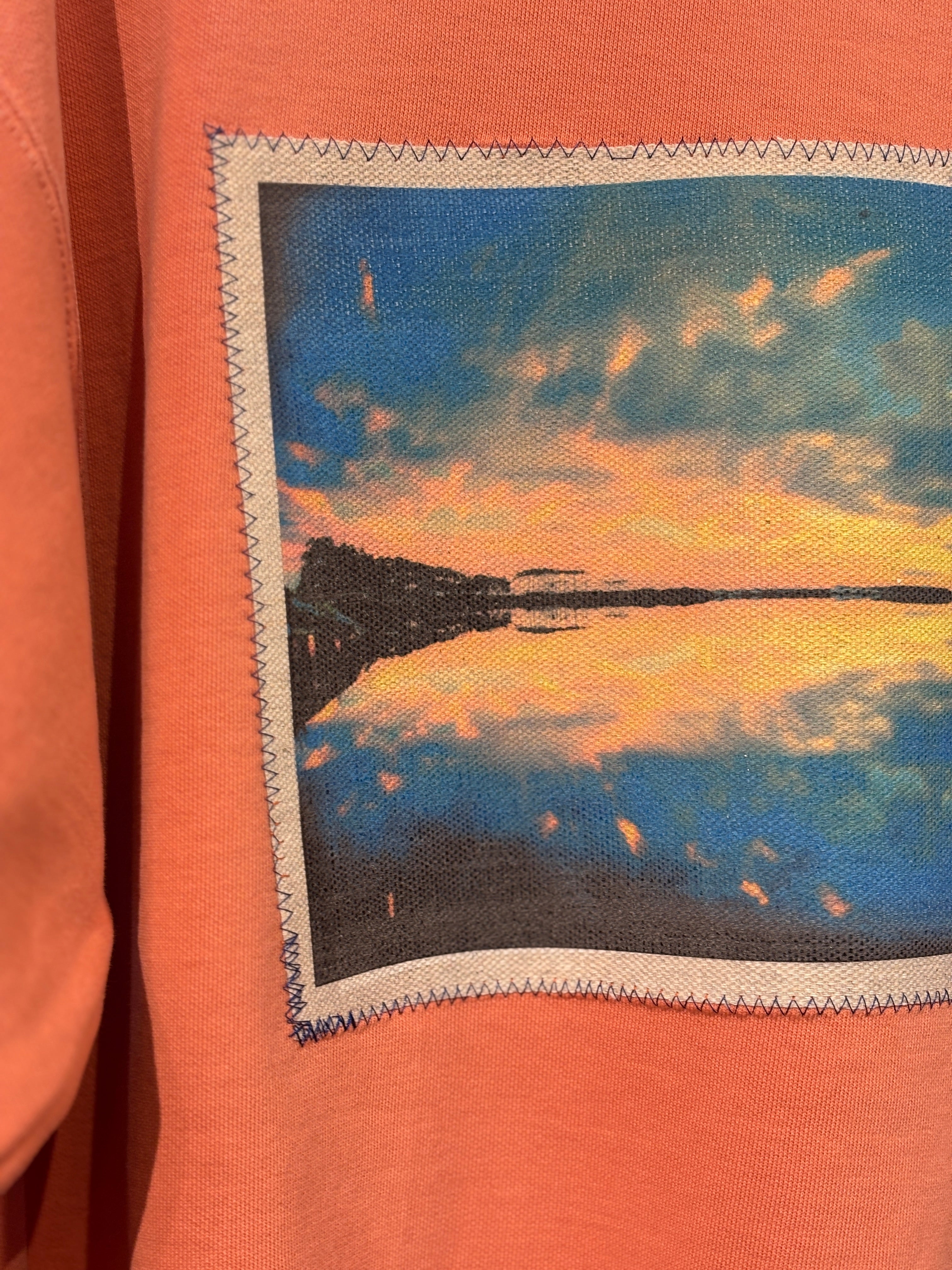 Orange sweatshirt with a photo of a sunset over a lake.
