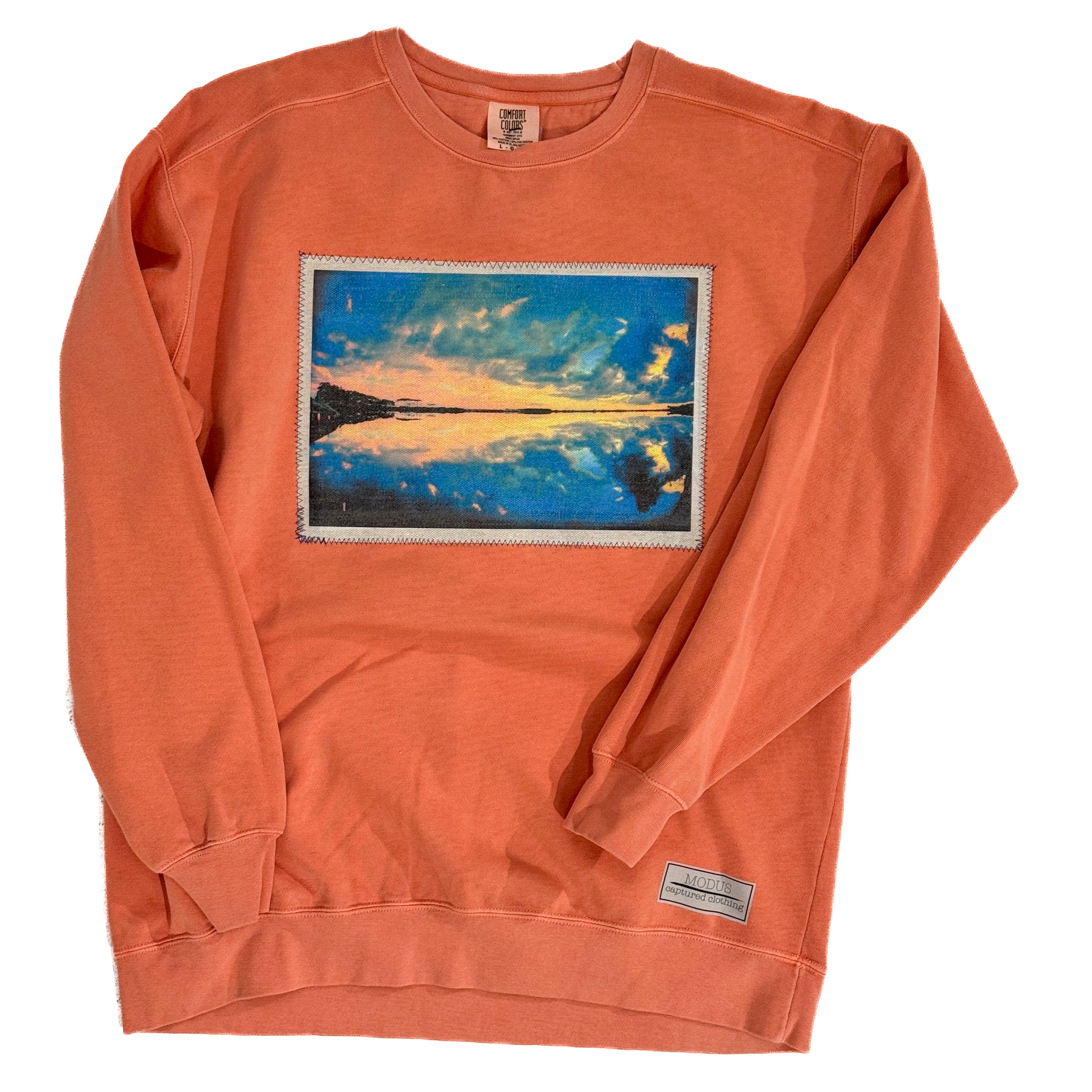 Orange sweatshirt with a printed design of a sunset over water on a white background