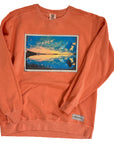 Orange sweatshirt with a printed design of a sunset over water on a white background