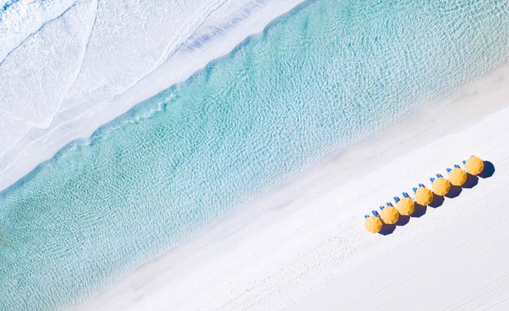 Aerial view of yellow beach umbrellas along turquoise Gulf water and white sand on Florida’s 30A coast.