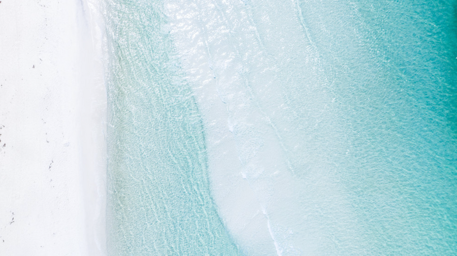 Aerial photo showing turquoise Gulf water blending into white sand along Florida’s 30A coast.