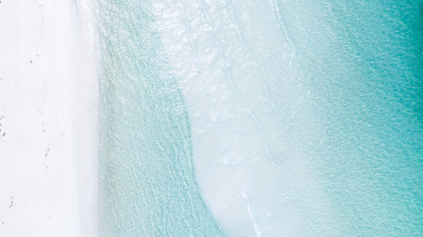 Aerial photo showing turquoise Gulf water blending into white sand along Florida’s 30A coast.