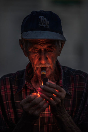 Elderly Cuban man lighting a cigar in low morning light, portrait photograph by Chandler Williams.