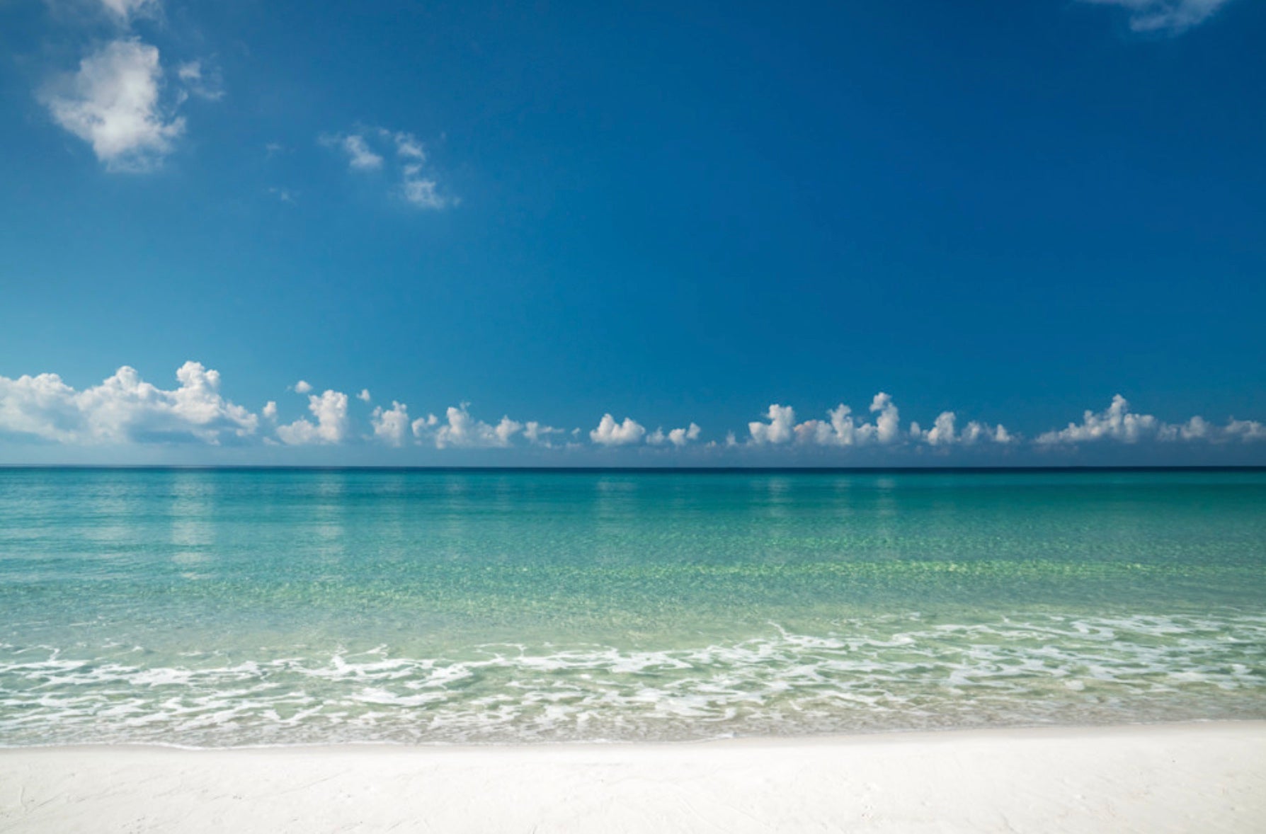 Turquoise Gulf water and white sand under a clear blue sky on Florida’s Emerald Coast.