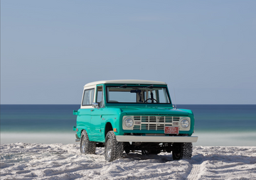 Vintage turquoise Bronco parked on white sand beach with Gulf backdrop in Grayton Beach.