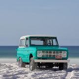 Vintage turquoise Bronco parked on white sand beach with Gulf backdrop in Grayton Beach.