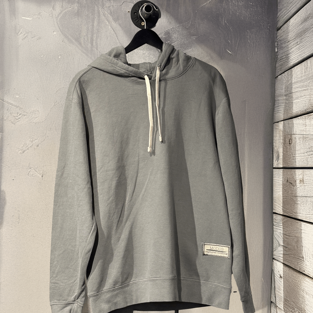 Gray hoodie on a hanger against a textured wall with a modus captured clothing tag on it. 