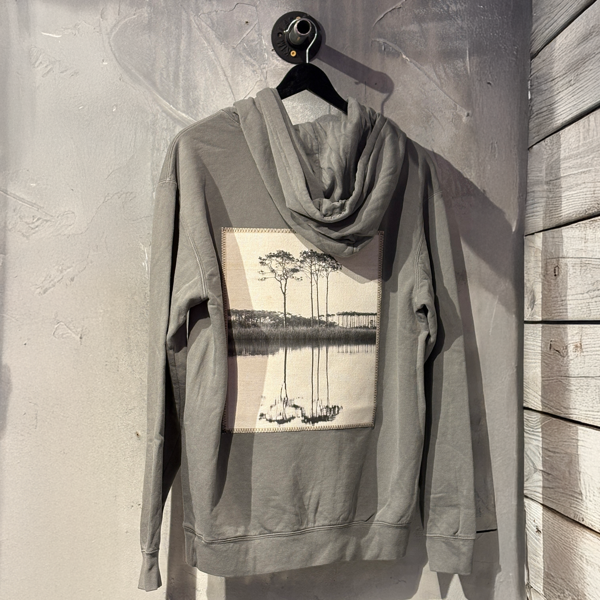 Gray hoodie with a nature-themed graphic on a hanger against a textured wall.