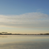 Sunrise photograph of Western Lake with calm water reflecting blue sky and longleaf pines, Grayton Beach Florida.