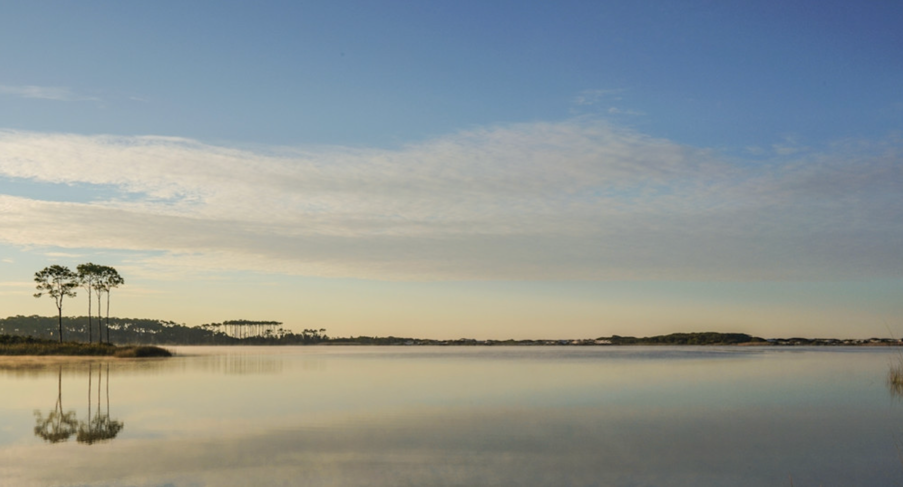 Sunrise photograph of Western Lake with calm water reflecting blue sky and longleaf pines, Grayton Beach Florida.